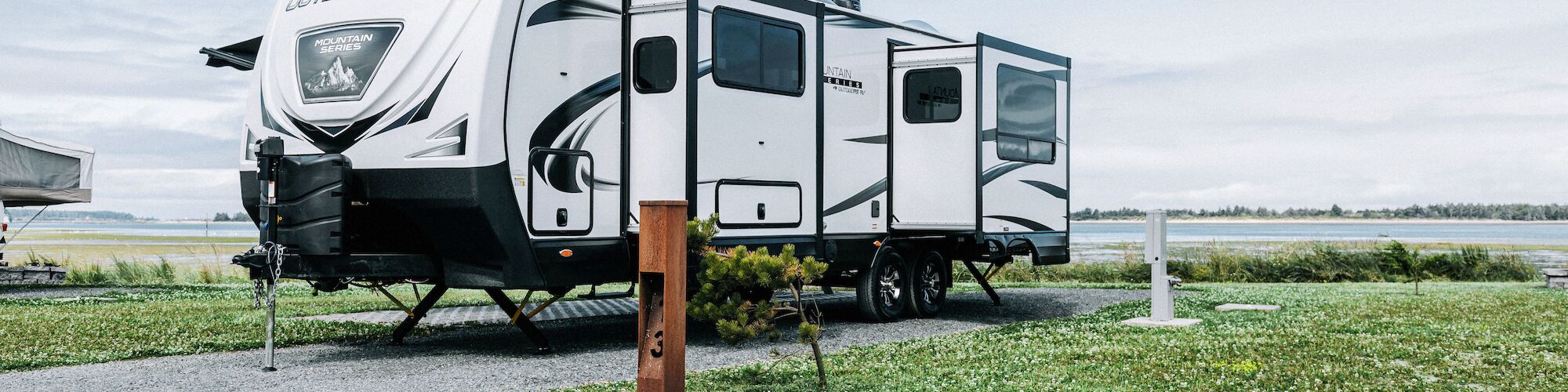 A large RV parked on a grassy area near a water source, with a cloudy sky in the background.