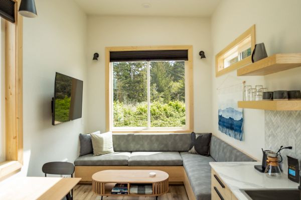 A cozy kitchen and living area with modern furnishings, a skylight, large window, seating, a table, and wall-mounted TV.