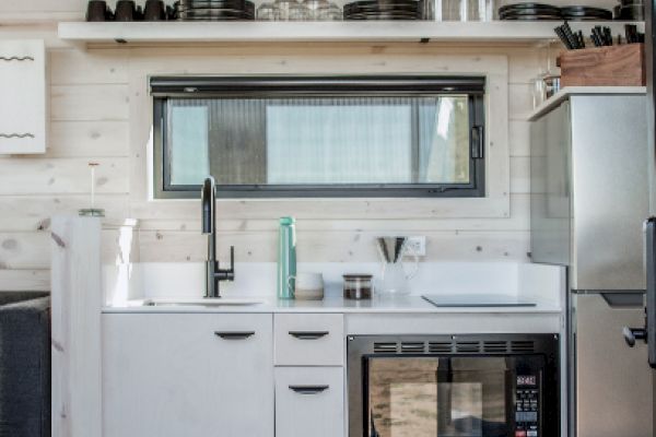 A compact kitchen with white cabinetry, a sink, stove, and a mini-fridge. Shelves hold cookware and utensils above. Cozy and efficient design.