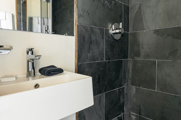 A modern bathroom features a sink with exposed plumbing and a shower with dark tile walls and a pebble floor.