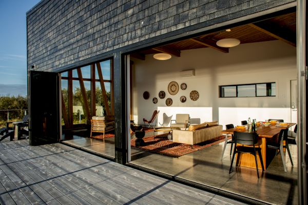 A modern open living and dining space with large glass doors leading to a wooden deck, featuring stylish furniture and wall decorations.