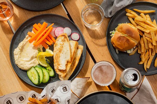 A table with dishes of fries, burgers, salad, wraps, and drinks on black plates, garnished with veggies and sauces.