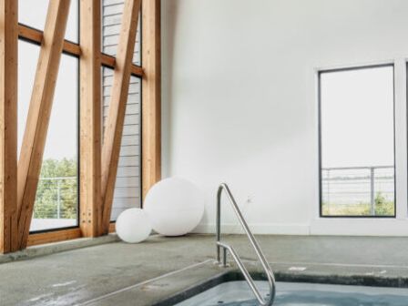 The image shows an indoor pool with a metal handrail, large windows, and spherical white decorations on the floor nearby.