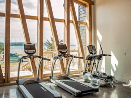 A gym room with three treadmills faces large wooden-framed windows, offering a view of the outdoors.