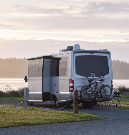 A camper van parked near a scenic lakeside, featuring attached bicycles and a beautiful sunset in the background.