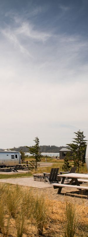 The image shows a sunny day with two silver Airstream trailers, picnic tables, and sparse landscape.