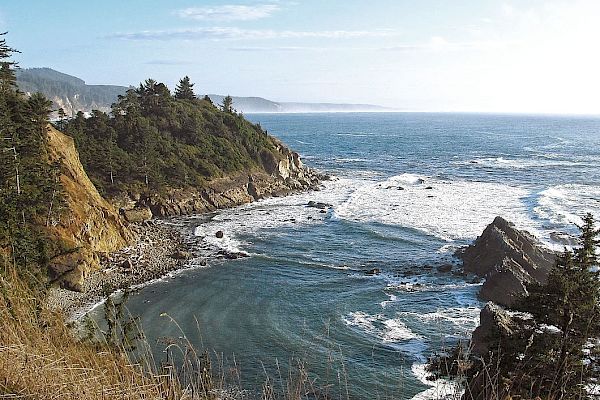 A scenic coastal view with rocky cliffs, waves crashing below, and a clear blue sky above the ocean horizon.