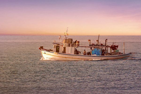 A fishing boat sails on calm waters under a colorful twilight sky, creating a serene and picturesque scene.