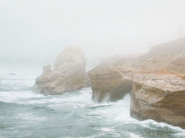 A foggy coastal scene with rocky cliffs and waves crashing against the shore, creating a serene and misty atmosphere.