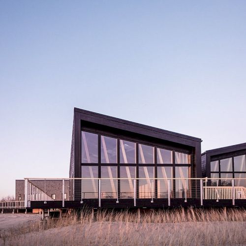 A modern building with angular design and large windows, set in a grassy landscape under a clear sky.