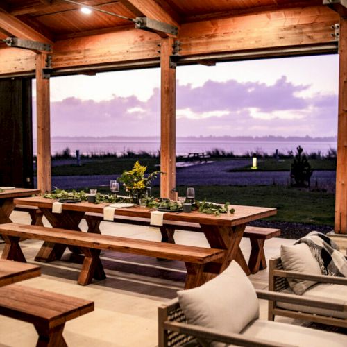 A cozy outdoor dining area with wooden tables and benches, overlooking a scenic view of the ocean at sunset.