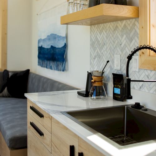 A modern kitchen with a sleek countertop, black faucet, wooden cabinets, and a cozy seating area in natural light.