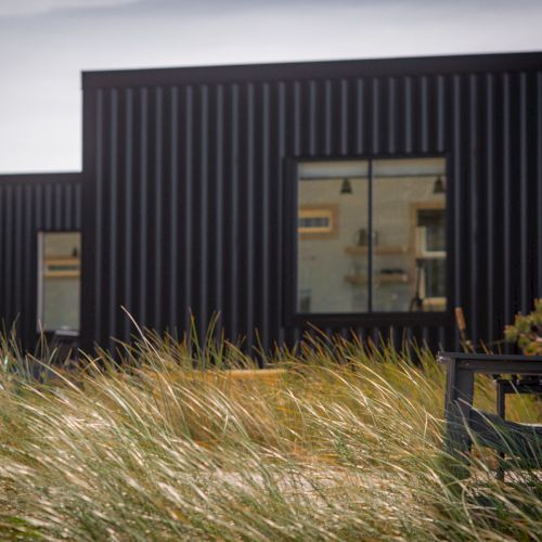 A modern building with dark walls sits behind tall grass, and an empty black chair is visible in the foreground.