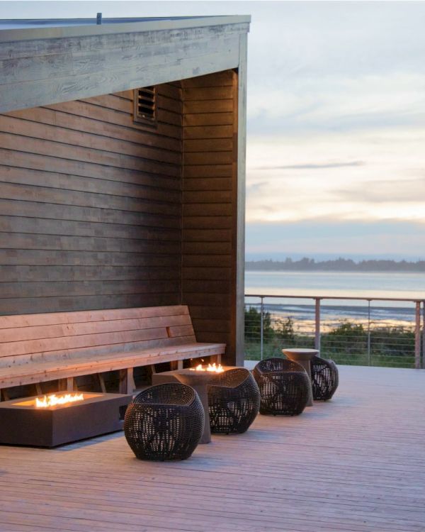 Outdoor seating area with a wooden bench, decorative fire pits, and an ocean view. The scene is calm and inviting with a modern design.