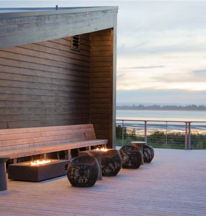 A modern outdoor patio with a wooden bench, decorative pots, and a scenic view of the water and distant landscape during sunset.