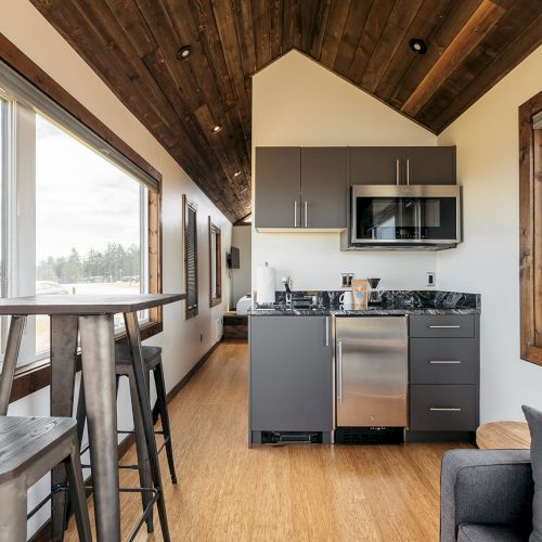 The image shows a modern, compact kitchen in a tiny house with a small dining area and wooden accents.