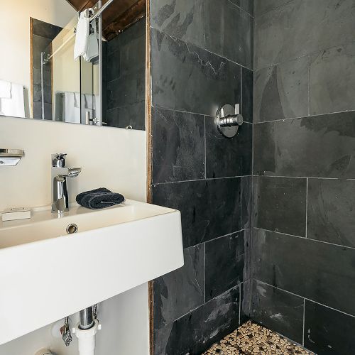 The image shows a modern bathroom with a white sink, slate tile shower, and pebble stone shower floor, featuring a rain showerhead.