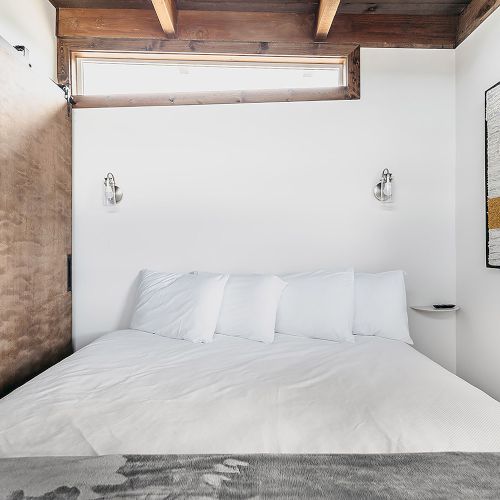 A cozy bedroom with a large bed, white bedding, wooden sliding door, wall art, and ambient wall lights.