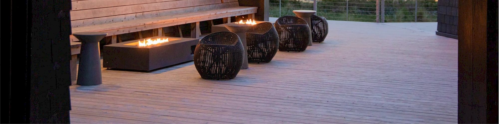 A stylish outdoor deck with modern seating, ambient lighting, and a scenic view of the horizon at dusk, featuring neat wooden architecture.