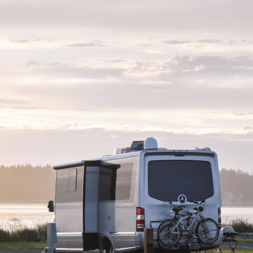 A camper van with bicycles on the back parked near a lake or sea at sunset.