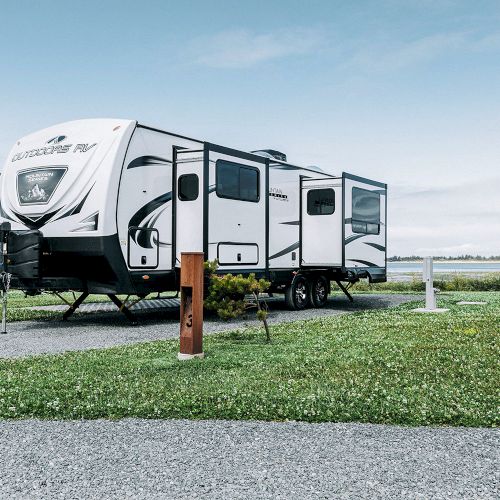 A white travel trailer parked on gravel near green grass and open sky, showcasing a peaceful camping setting.