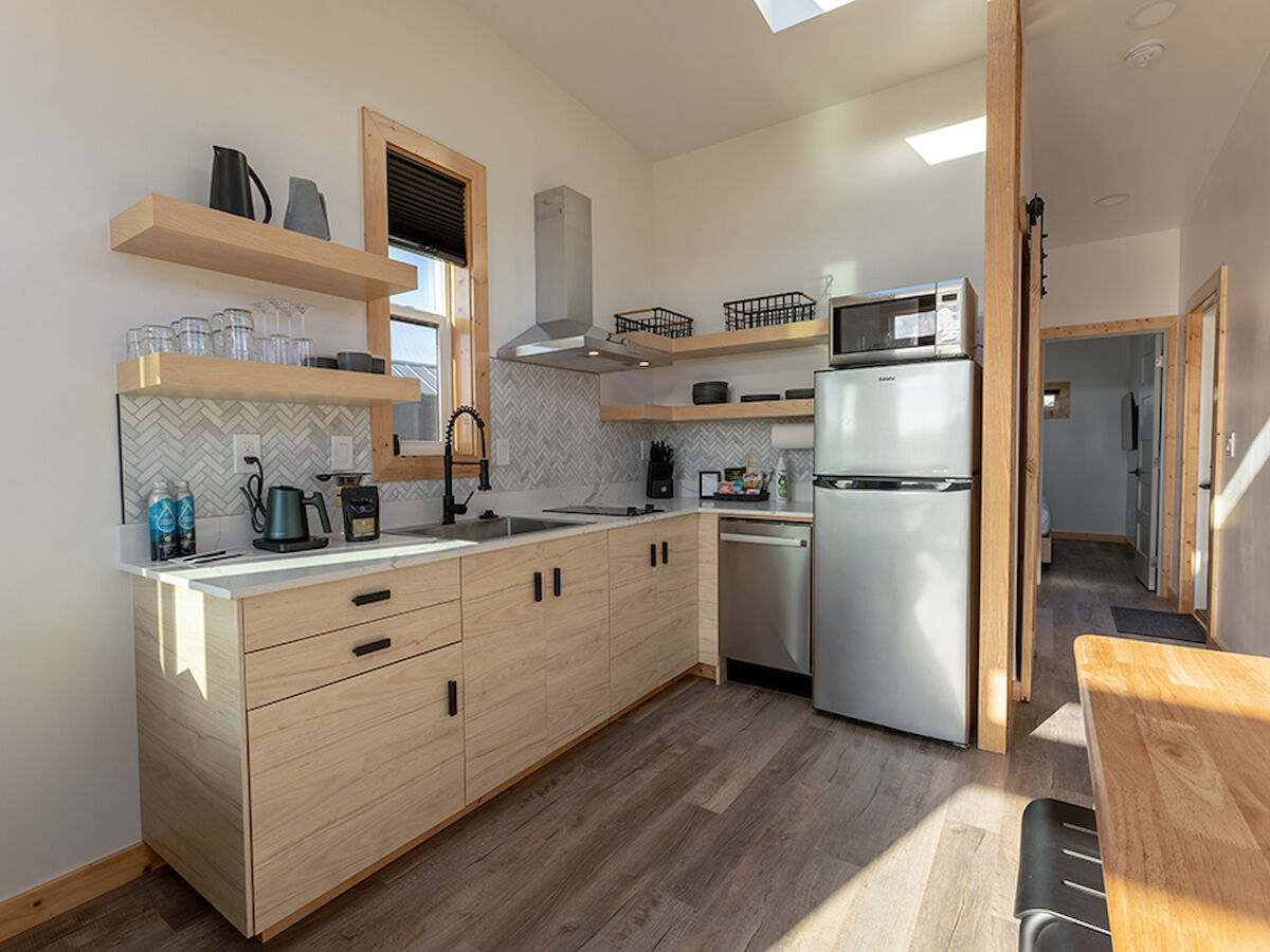 A modern kitchen with light wood cabinetry, stainless steel appliances, open shelving, and ample counter space.