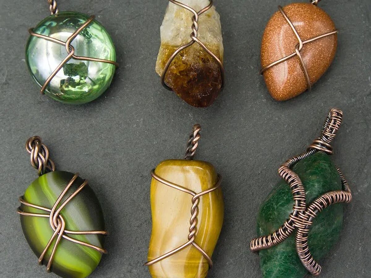 The image shows six colorful stones wrapped in wire designs, laid out in two rows of three on a dark surface.