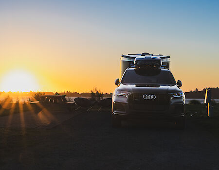 A car is parked on a road during sunset, with a clear sky and trees in the background.