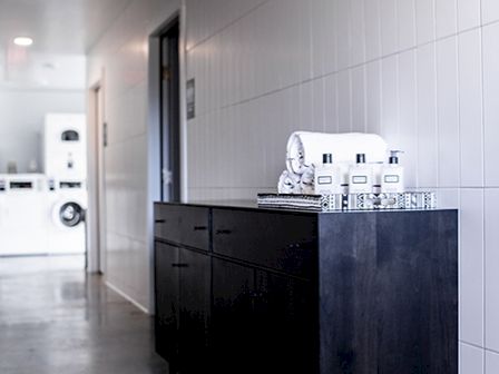 The image shows a hallway with a dark cabinet on the side, a coffee machine on top, and a white door in the background leading to a laundry room.