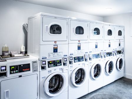 A clean laundry room with a row of stacked front-loading washers and dryers is shown against a white wall.