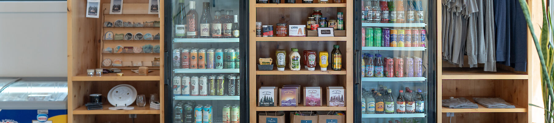 The image shows shelves with drinks, apparel, and gifts, plus three fridges stocked with cans and bottles.