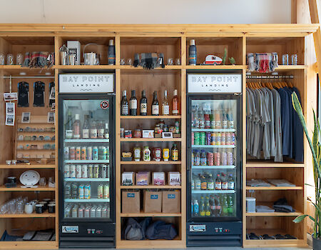 The image shows shelves with drinks, apparel, and gifts, plus three fridges stocked with cans and bottles.