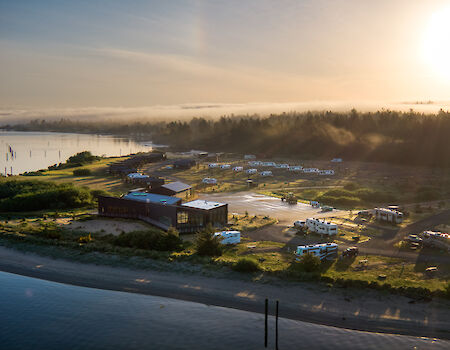 Aerial view of a campsite with RVs near a river and forest, under a sunrise or sunset sky.